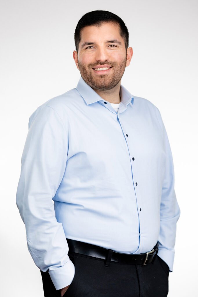 Yassin Bouzzin, Nachhaltigkeitsberater bei Systain: lächelnder Mann in hellblauem Hemd mit Händen in den Hosentaschen